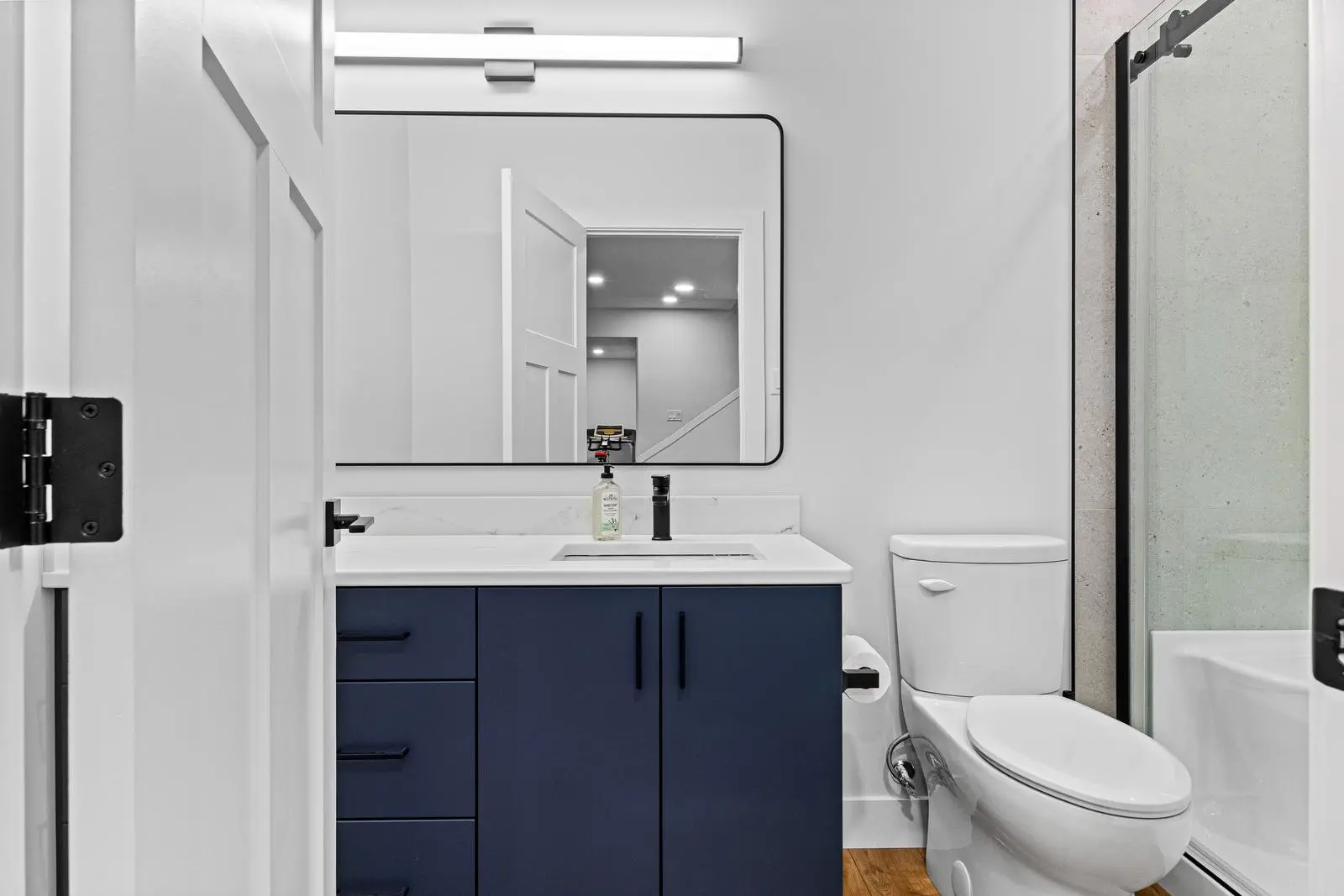 Bathroom renovation features navy vanity, walk-in glass shower.