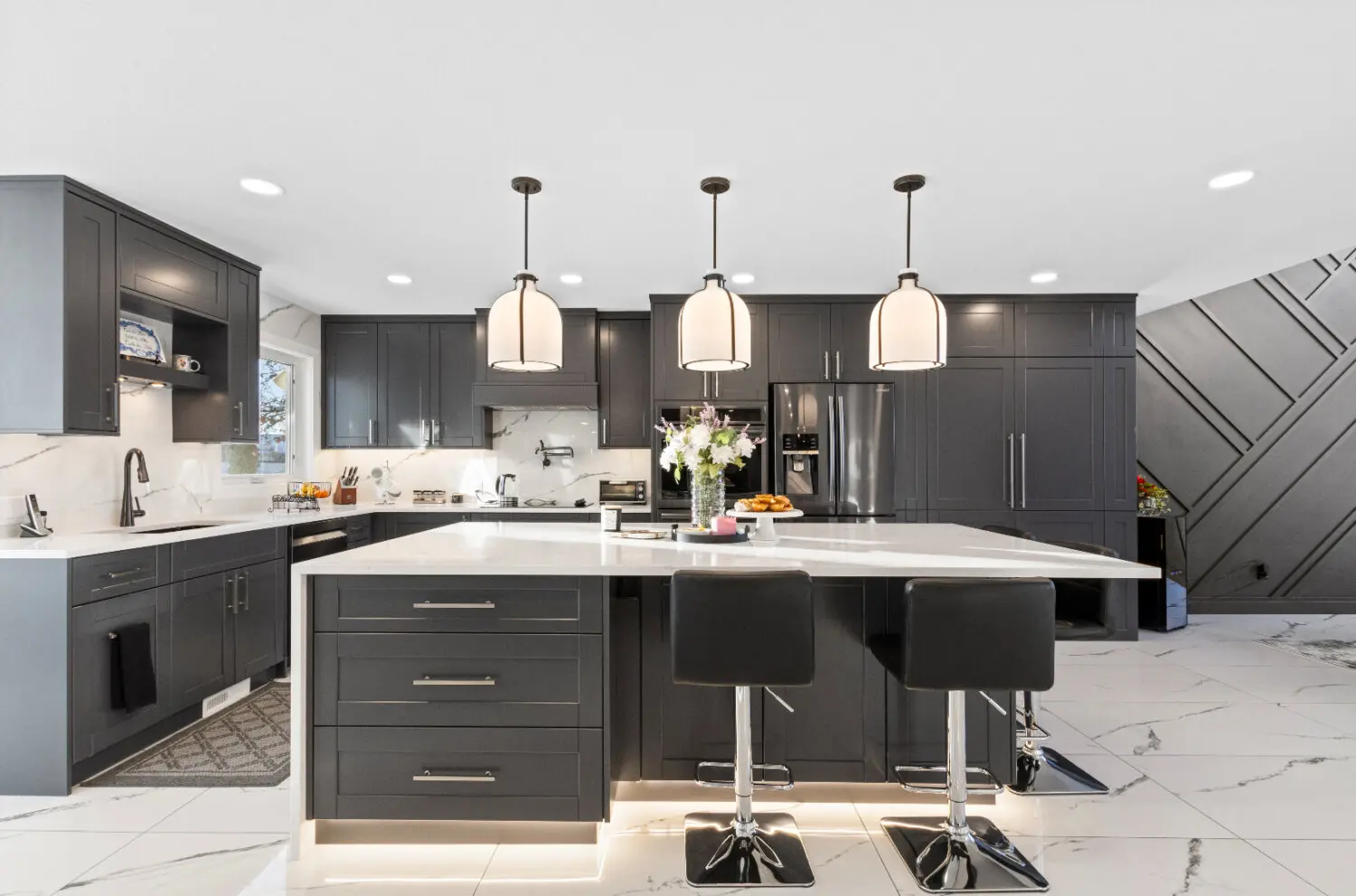 Kitchen renovation features dark cabinets, marble island, pendant lighting.
