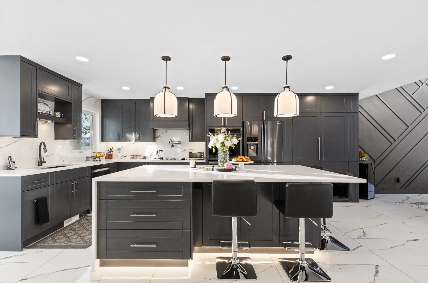 Kitchen renovation features dark cabinets, marble island, pendant lighting.